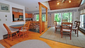A spacious kitchen with wooden cabinets, a dining area with chairs, and a large window providing a view of greenery. - Sunrise by Taylor Made Deep Creek (Oakland)
