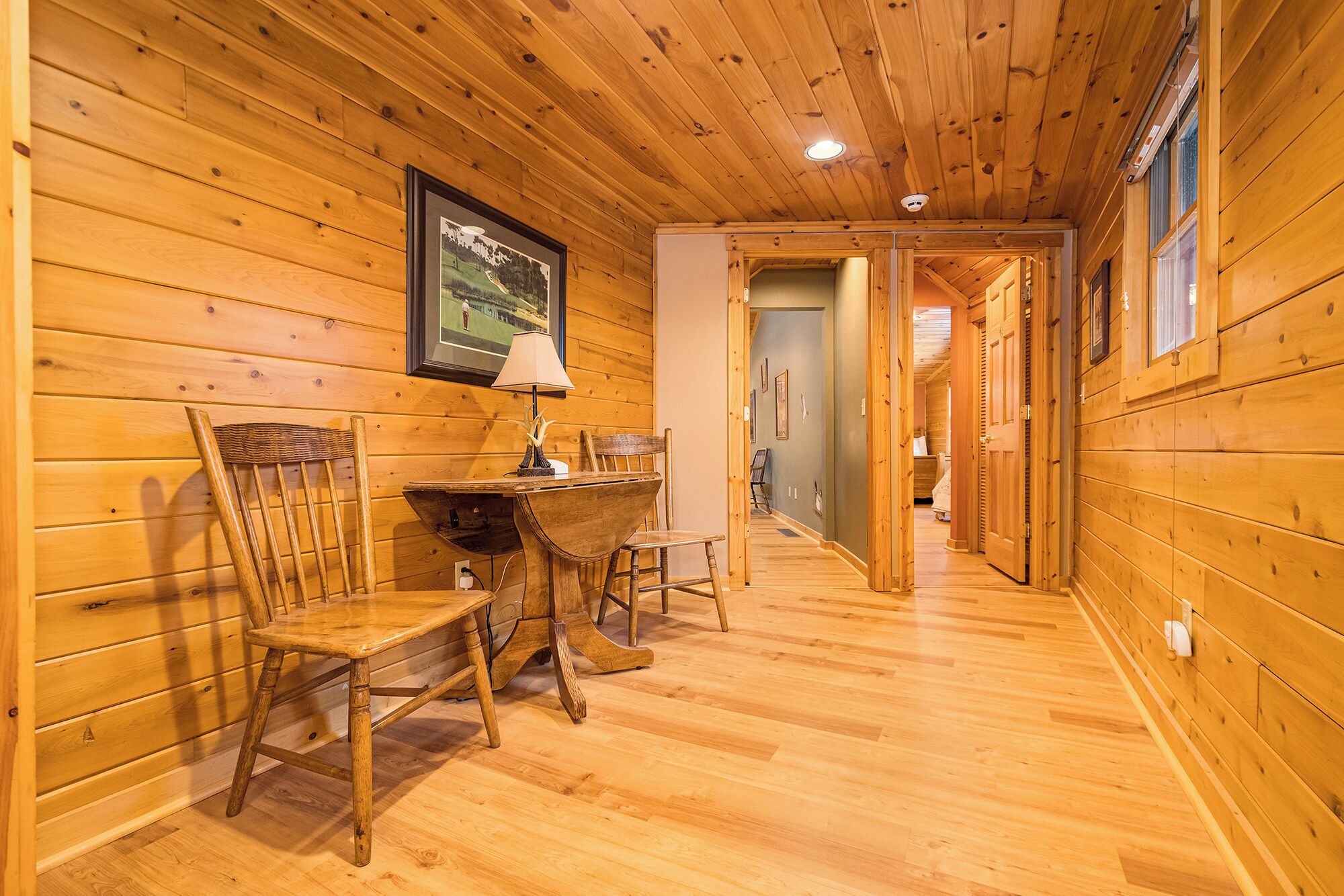 Un interior de madera con una zona de comedor, un cuadro en la pared y un pasillo que conduce a otra habitación.