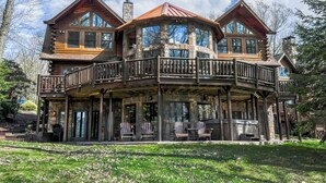 Eine Blockhütte mit Balkon, großen Fenstern und einem Steinkamin.