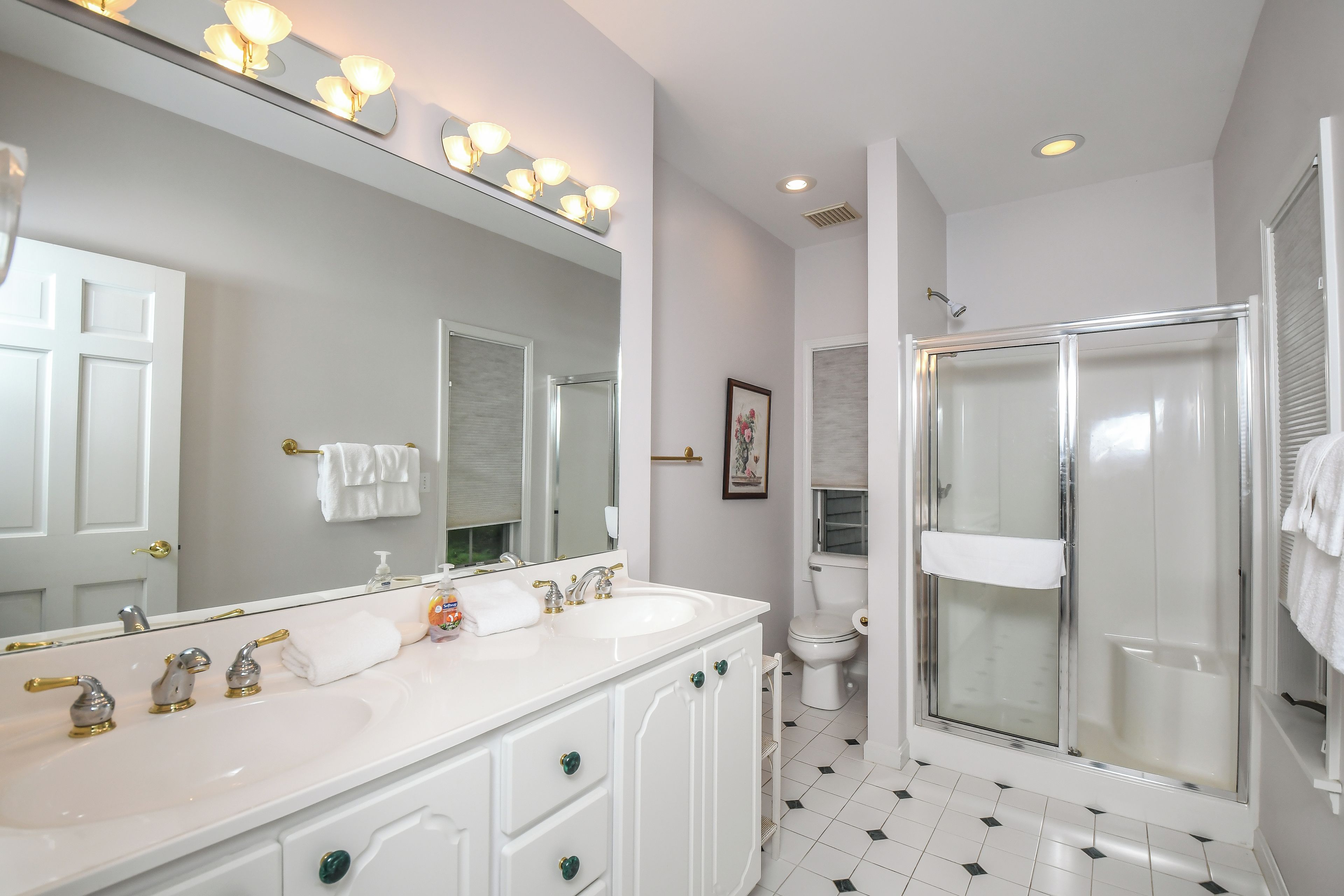 A bathroom with a large mirror, two sinks, a shower, and a toilet.