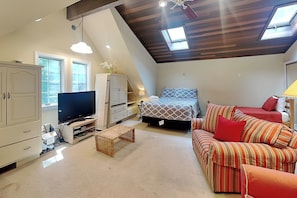 Un dormitorio estilo loft con techo inclinado, una cama, un sofá, un televisor y un escritorio.