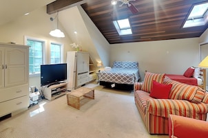 A loft-style bedroom with a sloped ceiling, a bed, a sofa, a TV, and a desk.