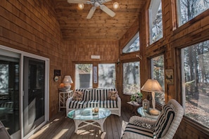 A wooden cabin interior with a glass table, striped sofa, and wicker chairs. - Sunset View by Taylor Made Deep Creek (Swanton)