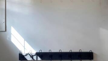 A white air conditioner mounted on a wall, a black shelf with hooks below it, and a whiteboard to the left.