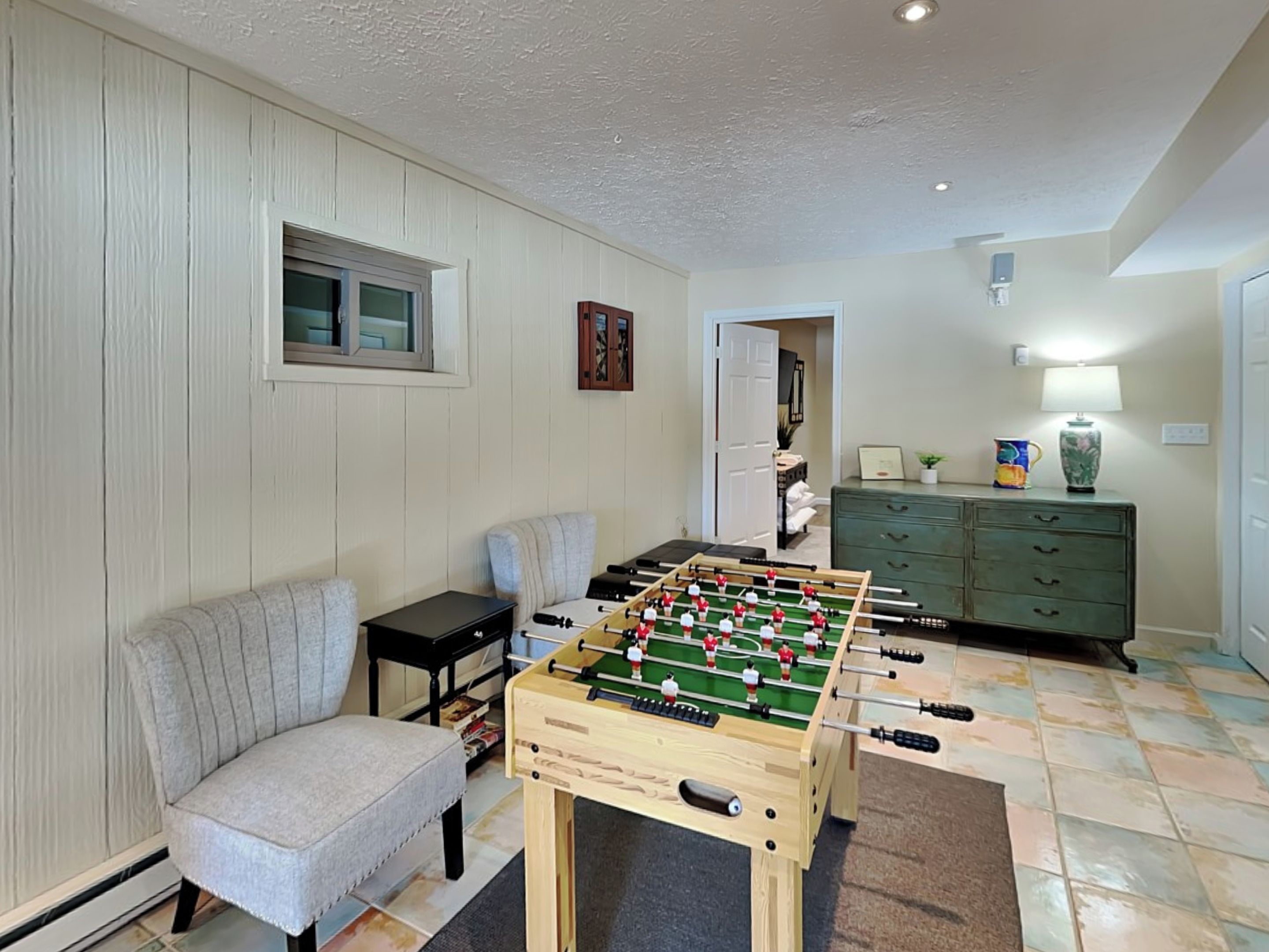 A cozy living room with a foosball table, a comfortable armchair, and a green cabinet.