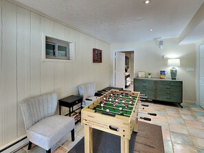 A cozy living room with a foosball table, a comfortable armchair, and a green cabinet. - Swan's Nest by Taylor Made Deep Creek (Swanton)