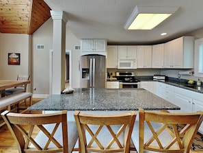A modern kitchen with a granite island, white cabinets, stainless steel appliances, and wooden chairs. - Penn Point Paradise by Taylor Made Deep Creek (Oakland)
