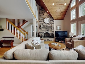 A spacious living room with a stone fireplace, a large clock, and a TV. - Penn Point Paradise by Taylor Made Deep Creek (Oakland)