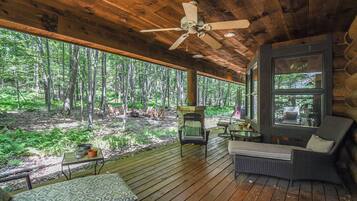 A wooden deck with a ceiling fan, wicker furniture, and a view of a forest.