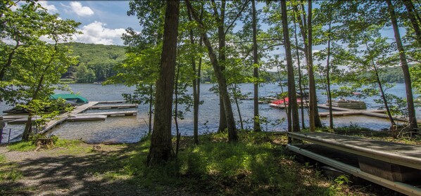 A lakeside view with docked boats, a wooden bench, and a forested area.