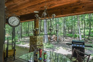 A rustic wooden structure with a hanging clock, a stone fireplace, and a barbecue grill. - Tao House at Serenity Woods by Taylor Made Deep Creek (McHenry)