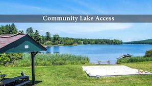 A lakeside community access area with picnic tables, a covered shelter, and a sandy area for beach activities.