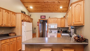 A kitchen with wooden cabinets, a refrigerator, a microwave, and a stove. There are two stools at the island.