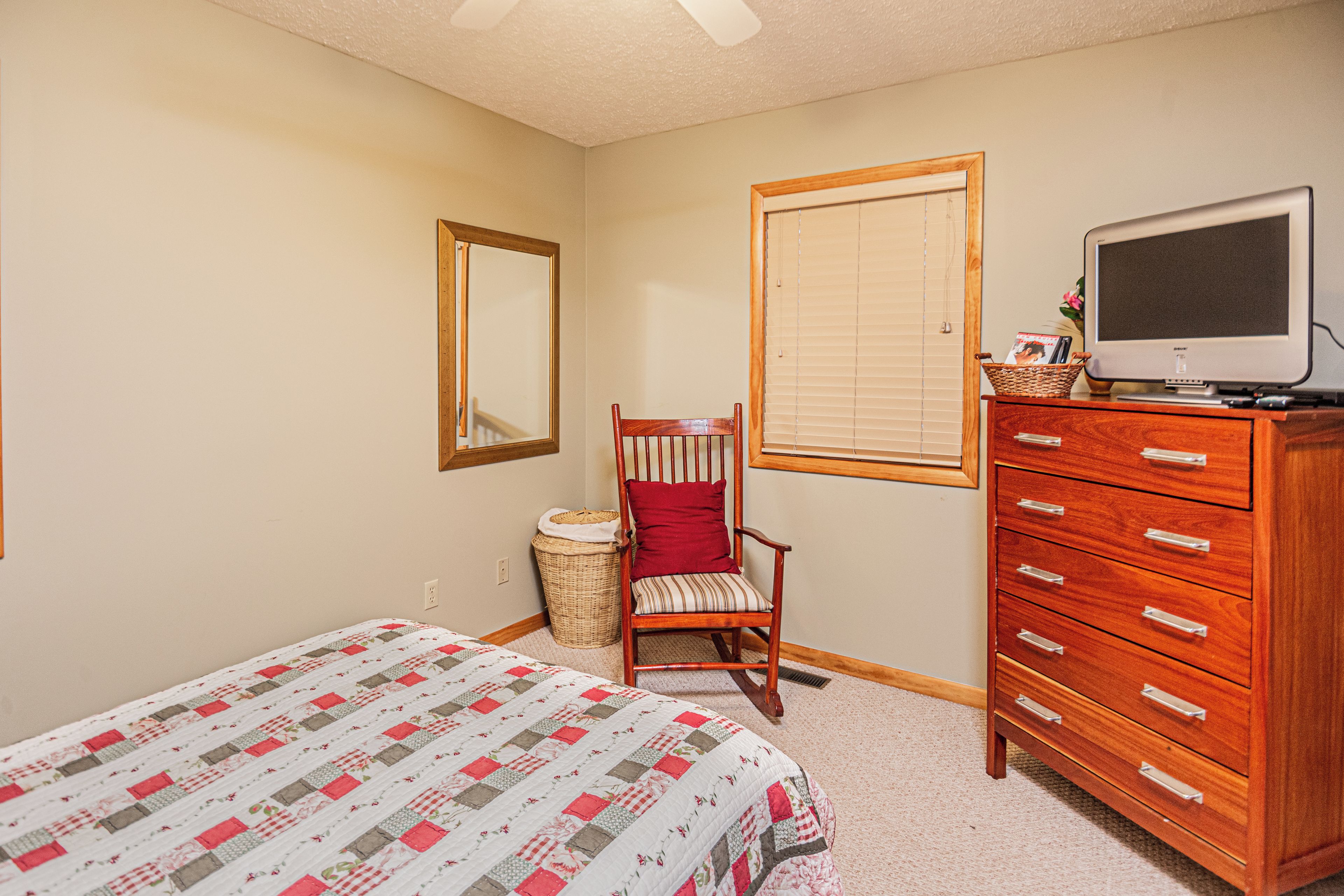 A bedroom with a bed, a wooden dresser, a chair, a television, and a window with blinds.