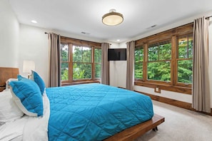 A bedroom with a large bed, two windows, a flat-screen TV, and a ceiling light. - The Haven by Taylor Made Deep Creek (Oakland)