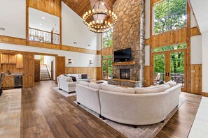 A spacious living area with a stone fireplace, wooden ceiling, and large windows.