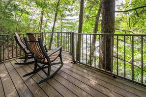A wooden deck with a metal railing, two rocking chairs, and a view of a forested area.