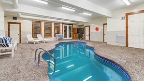 An indoor swimming pool with a tiled edge, lounge chairs, and a door leading to another room. - The Haven by Taylor Made Deep Creek (Oakland)