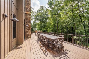 An outdoor deck with a wooden table and chairs, surrounded by a stone wall and metal railings. - The Haven by Taylor Made Deep Creek (Oakland)