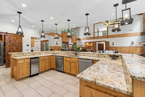 A spacious kitchen with granite countertops, wooden cabinets, and modern pendant lighting. - The Haven by Taylor Made Deep Creek (Oakland)