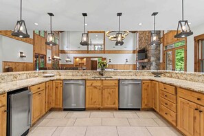 A spacious kitchen with granite countertops, stainless steel appliances, wooden cabinetry, and pendant lighting. - The Haven by Taylor Made Deep Creek (Oakland)