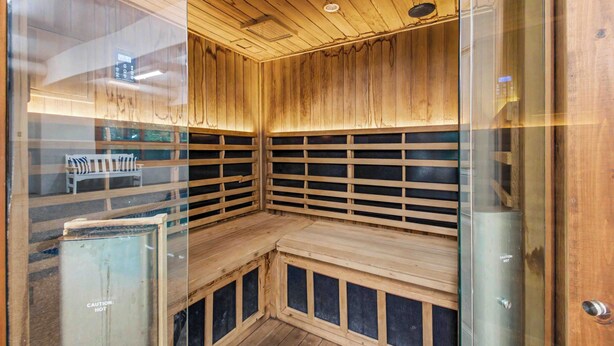 A sauna with wooden walls and benches, glass doors, and a ceiling with recessed lighting. - The Haven by Taylor Made Deep Creek (Oakland)