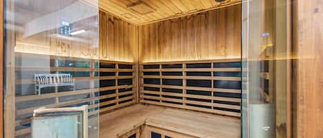 Una sauna con paredes y bancos de madera, puertas de cristal e iluminación empotrada en el techo.