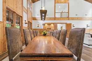 A long wooden dining table with leather-upholstered chairs, a vase of yellow flowers, and wooden paneling on the walls. - The Haven by Taylor Made Deep Creek (Oakland)
