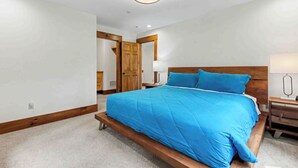 A bedroom with a large bed, wooden headboard, and a nightstand with a lamp. - The Haven by Taylor Made Deep Creek (Oakland)