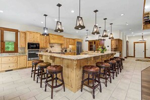 A spacious kitchen with wooden cabinets, a central island with stools, and pendant lighting. - The Haven by Taylor Made Deep Creek (Oakland)