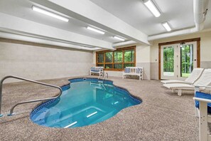 An indoor swimming pool with a clear view of the surrounding area, including a window with a view of trees and a door leading outside. - The Haven by Taylor Made Deep Creek (Oakland)