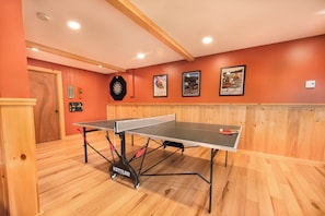 A ping pong table in a room with wooden floors and walls, a dartboard, and framed posters on the wall. - The Perch by Taylor Made Deep Creek (Oakland)