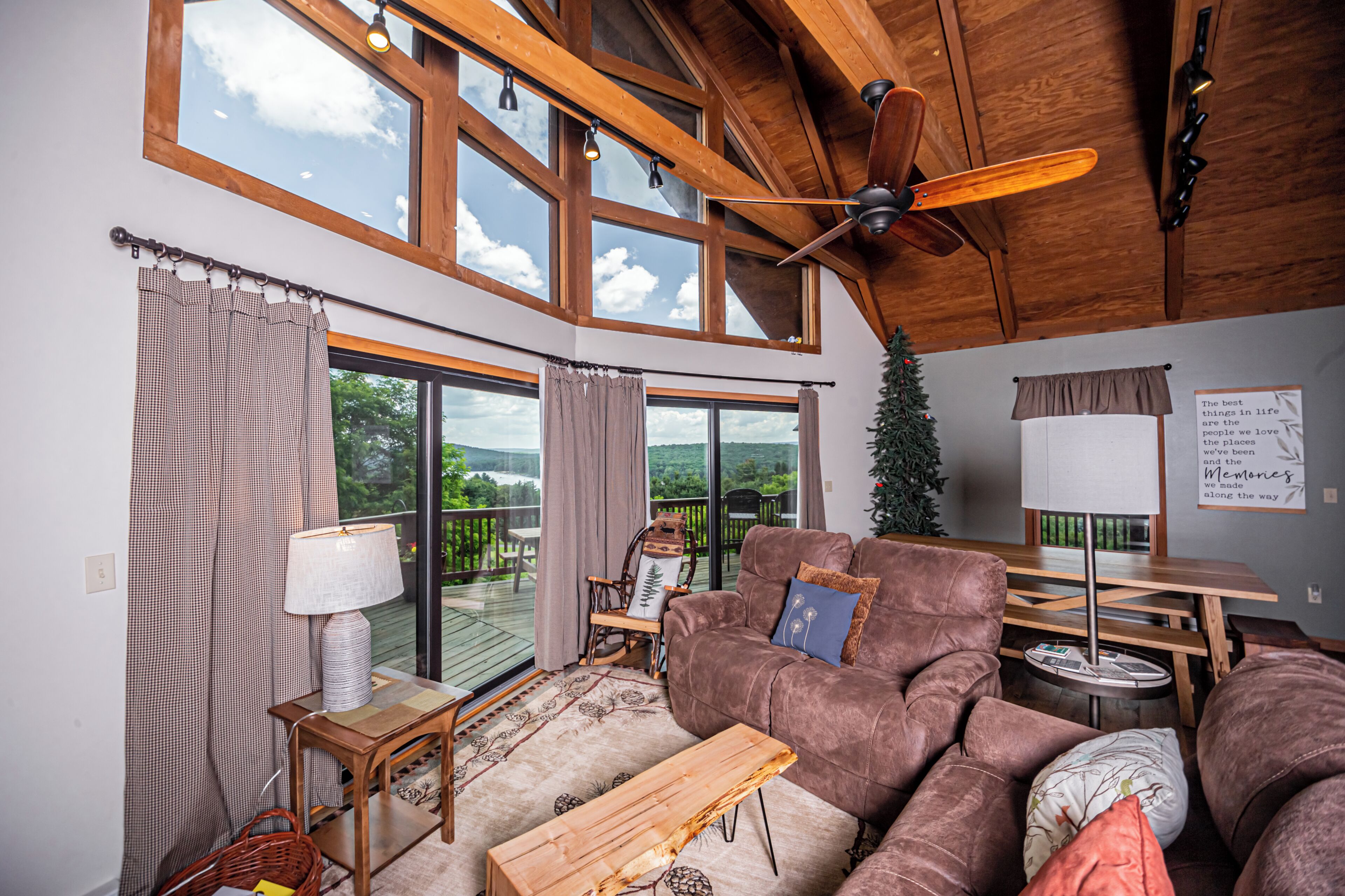 Un salon spacieux doté d’une grande fenêtre, d’un ventilateur de plafond, d’une table en bois et d’un coin salon confortable.