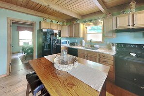 Une cuisine avec des meubles en bois, un réfrigérateur, un four à micro-ondes, un évier et une table à manger avec un panier.