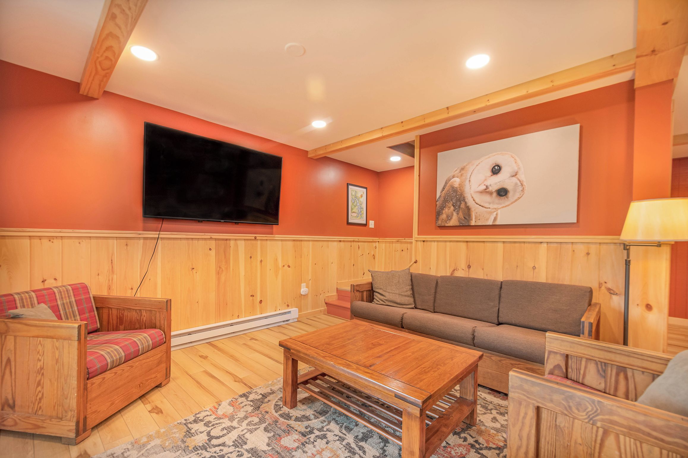 Una sala de estar acogedora con paredes de madera panelada, un televisor de pantalla plana, un cuadro grande de un búho y una mesa de centro de madera.
