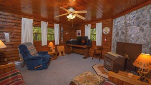 L’intérieur chaleureux d’un chalet avec un plafond en bois, un téléviseur, une cheminée et un coin salon confortable.