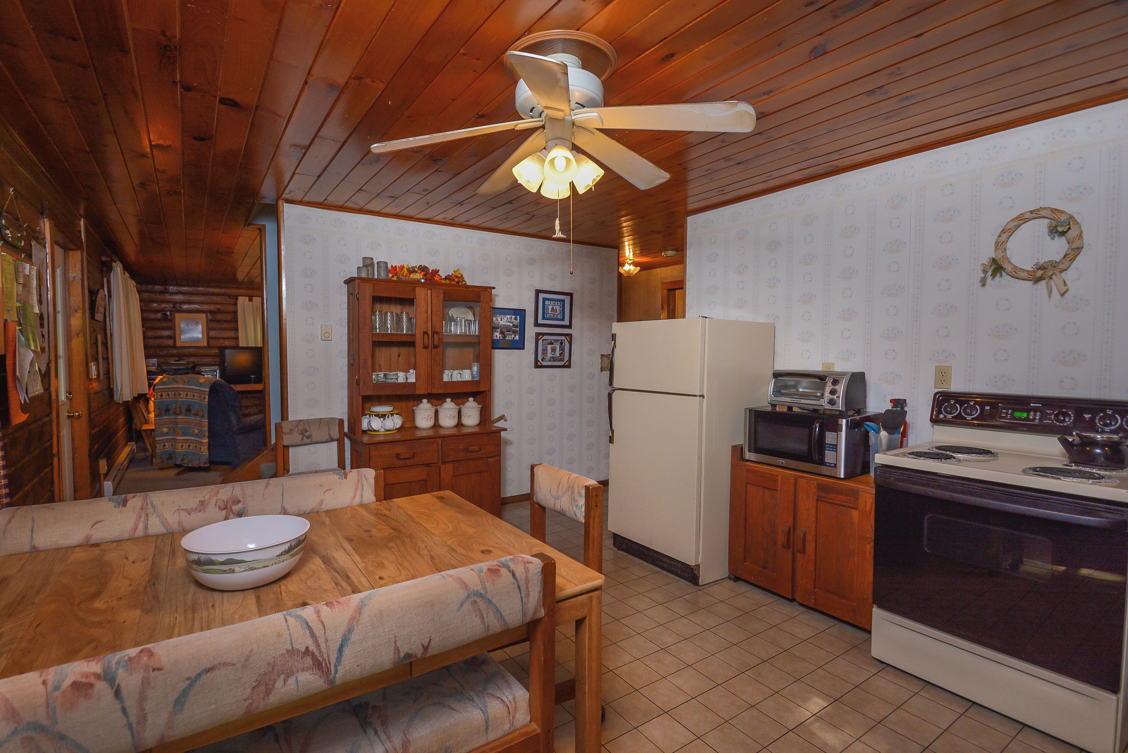 Ein Holzinterieur mit Esstisch, Stühlen, Deckenventilator, Kühlschrank, Mikrowelle und Herd.