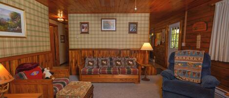 A cozy room with a plaid-patterned sofa, a blue armchair, a wooden bench, and a small table with a lamp.