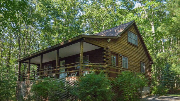 Une cabane en rondins dotée d’un porche couvert et d’un espace clôturé.
