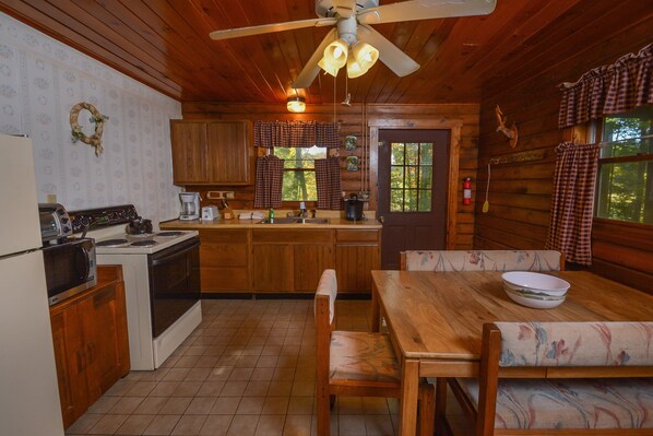 A cabin-style kitchen with wooden cabinets, a stove, and a dining area with a table and chairs. - The Pines by Taylor Made Deep Creek (Swanton)