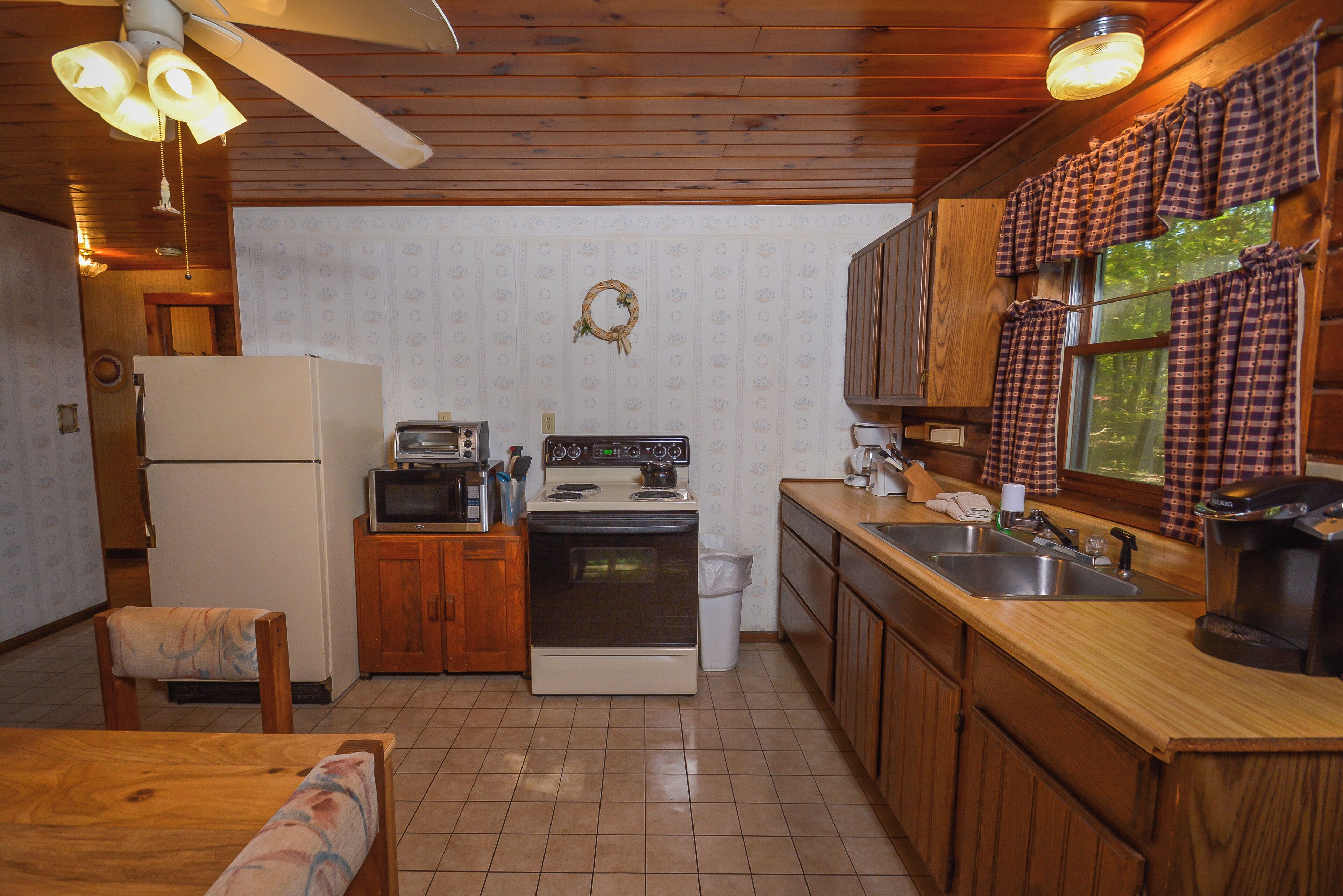 A compact kitchen with wooden cabinets, a refrigerator, a stove, a microwave, and a sink.