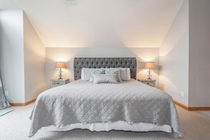 Une chambre à coucher avec un grand lit, deux tables de chevet avec des lampes et une tête de lit capitonnée.