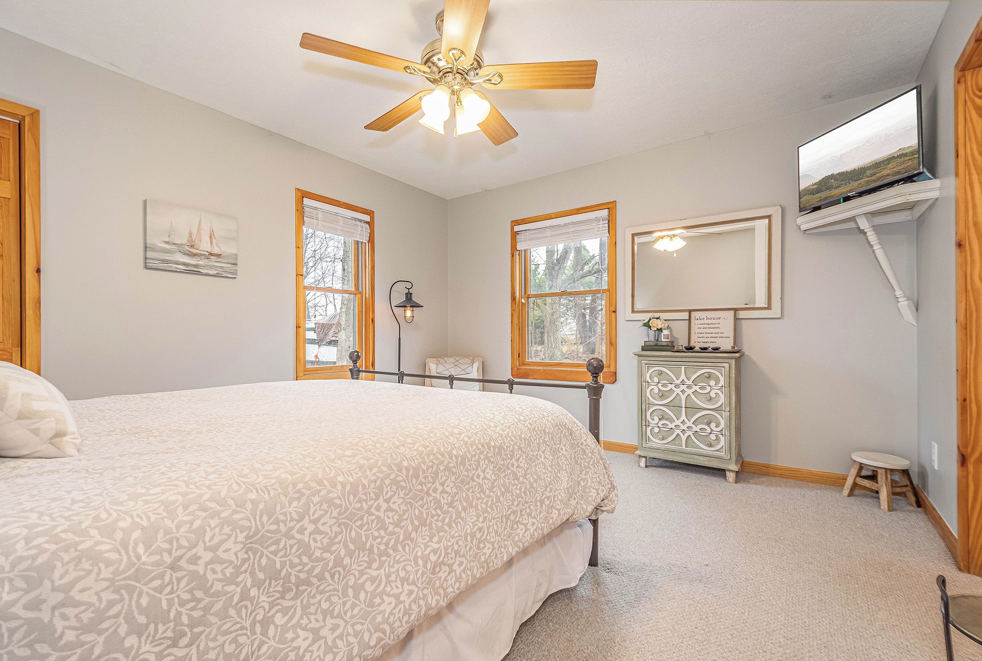 A bedroom with a bed, a ceiling fan, a dresser, a television, and windows.