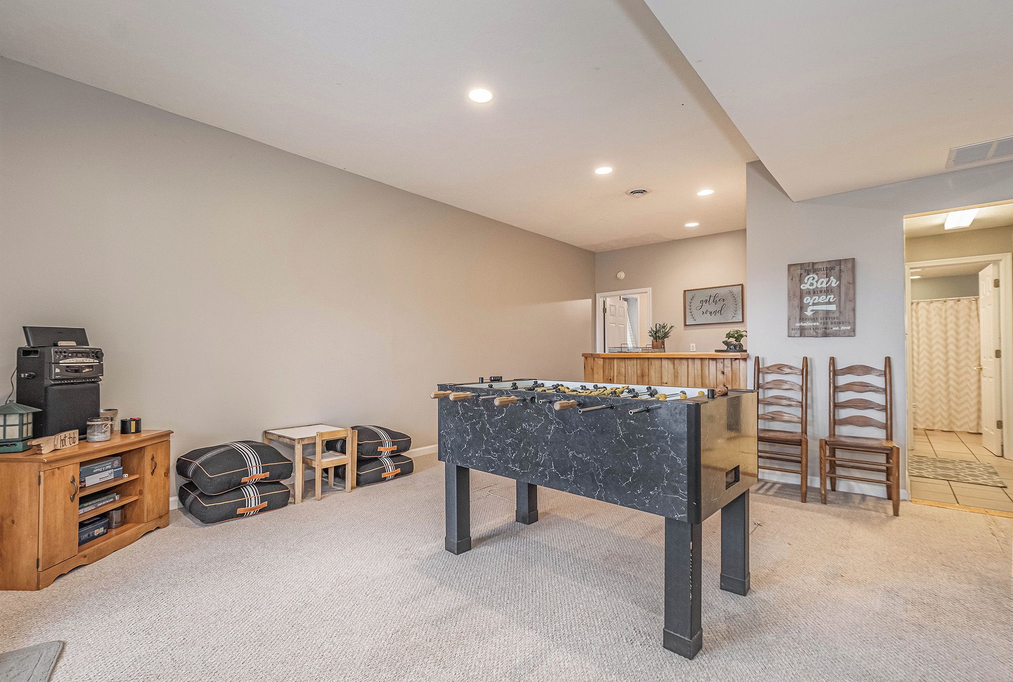 Una habitación con mesa de futbolín, un armario de madera y una pequeña mesa con una planta.
