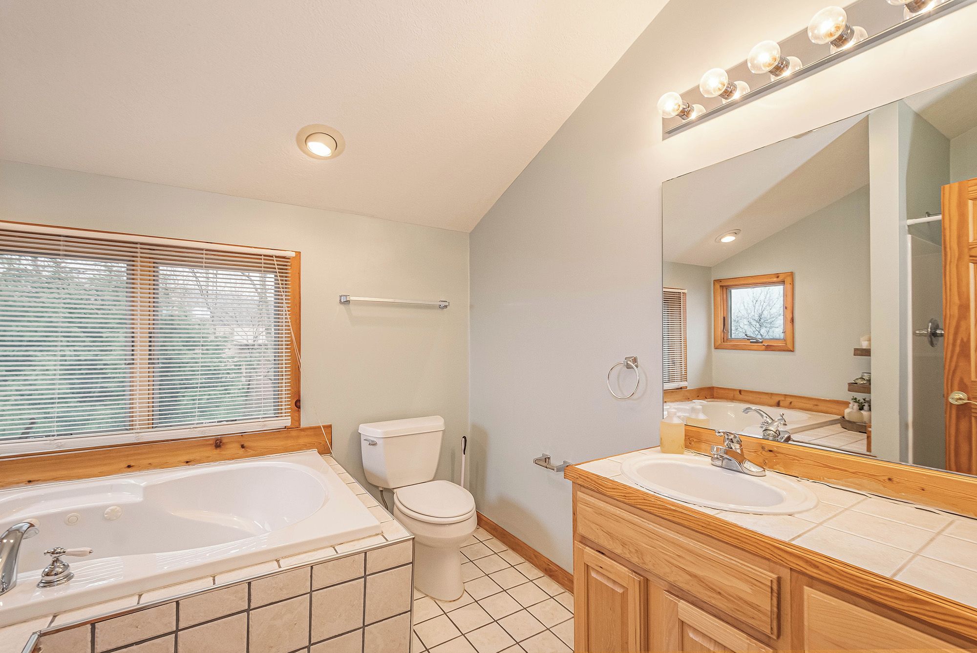 Une salle de bain avec une grande baignoire, deux lavabos, des toilettes et un miroir avec éclairage intégré.