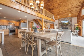 A spacious kitchen with wooden cabinets, a dining area with a table and chairs, a stone fireplace, and a living area with a sofa and TV.