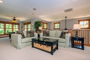 A living room with two light-colored sofas, a glass coffee table with wicker baskets, and a black side table with a lamp.