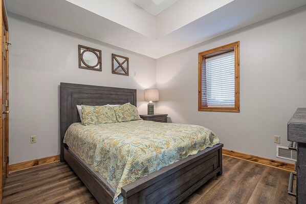 A bedroom with a bed, a nightstand, a lamp, a window with blinds, and a ceiling fan. - Under the Stars by Taylor Made Deep Creek (Oakland)