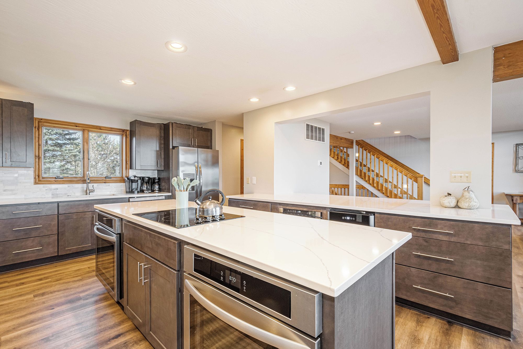 A modern kitchen with a large island, stainless steel appliances, and a wooden staircase.