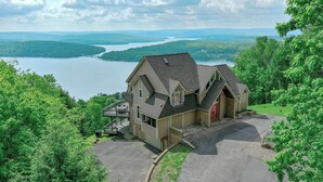 Une maison à deux étages dotée d’une grande véranda à l’avant, d’un patio couvert et offrant une vue sur un lac et des montagnes.